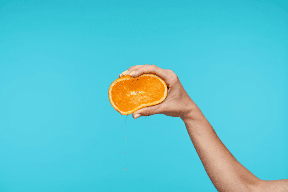 Hand squeezing orange to illustrate squeezing more value from success stories
